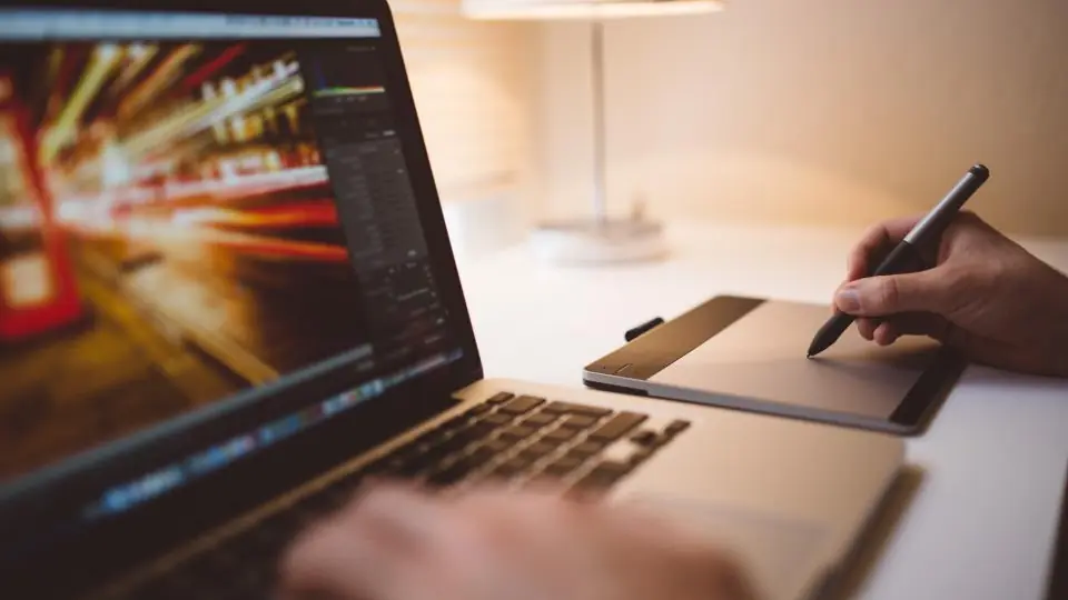 Someone editing a long-exposure photograph on a laptop while drawing on a pen tablet beside it.