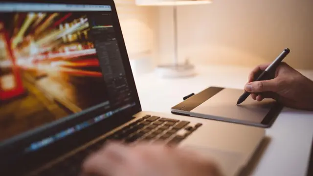 Someone editing a long-exposure photograph on a laptop while drawing on a pen tablet beside it.