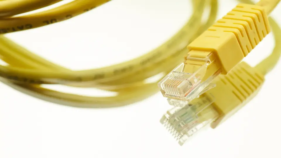 A coiled yellow Cat 5e patch cable on a white surface, with two RJ45 plugs in the foreground.